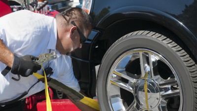 Tow truck driver with black sun glasses secures a vehicle onto his tow truck