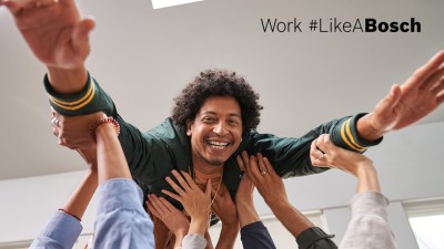 A Bosch employee with curly, brown hair "surfs" on the hands of many different colleagues.